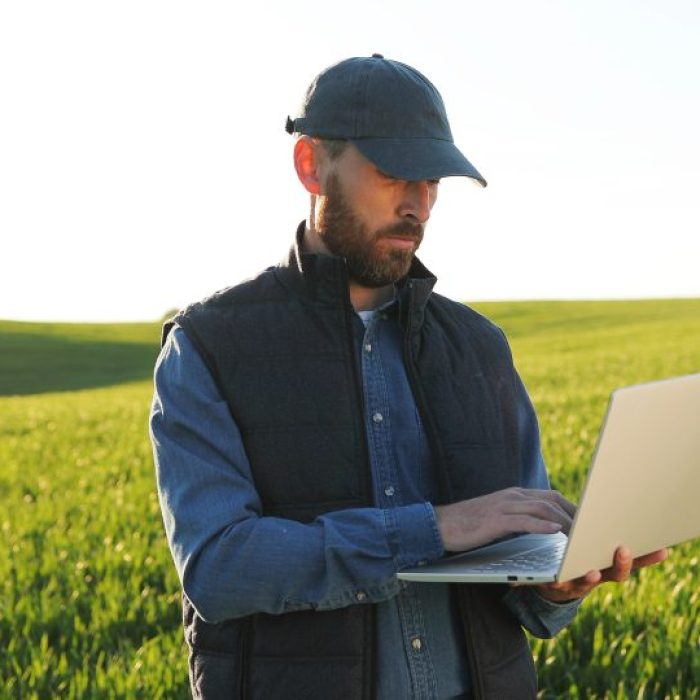 Caucasian Young Male Farmer In Hat Standing In Field And Typing